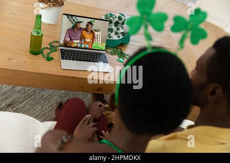 Coppia afroamericana che fa la videochiamata del giorno di san patrizio ad amici maschi felici sul laptop a casa Foto Stock