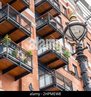 London warehouse condominio. Dettagli architettonici a telaio pieno di un vecchio edificio ristrutturato in contrasto con un palo di lampada a gas originale. Foto Stock
