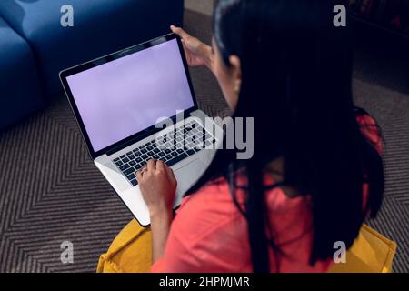 Vista ad alto angolo della giovane donna d'affari biraciale che utilizza un notebook con schermo vuoto che lavora in ufficio Foto Stock