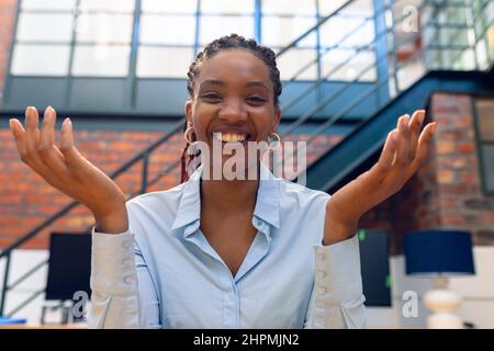 Ritratto di allegro afroamericano giovane donna d'affari gesturing mentre si siede in ufficio moderno Foto Stock