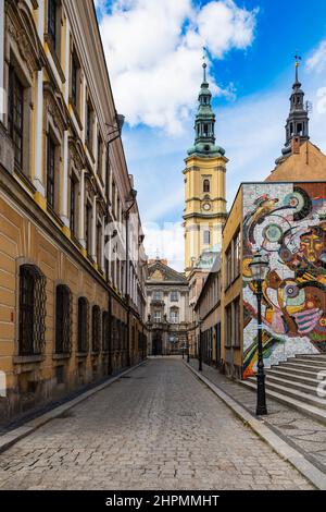 Legnica, Polonia - Aprile 2021: Torri di Parrocchia. Giovanni Battista a Legnica dietro l'edificio con mosaico colorato di Nicolaus Copernico sul muro Foto Stock