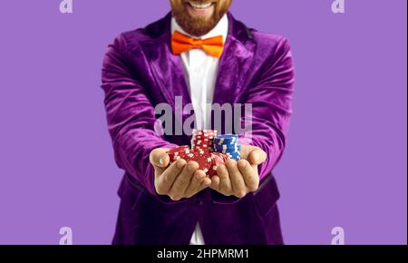 Primo piano di fiches di poker in mani di un uomo gioioso eccitato isolato su sfondo viola. Foto Stock