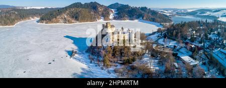 Polonia. Ampio panorama invernale aereo del lago artificiale ghiacciato di Czorsztyn con una diga e lago di ritenzione, castello medievale a Niedzica, risalente al 14t Foto Stock