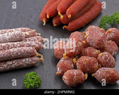 vari snacks di carne composizione, primo piano di salami mini essiccati all'aria serverale su piastra di ardesia nera Foto Stock