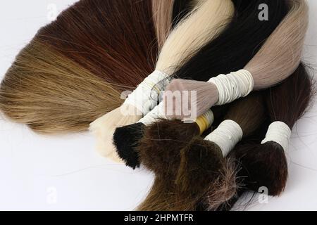 Campioni di capelli per l'estensione arrotolati, colori diversi.sfondo bianco. Foto Stock