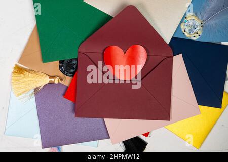 Cuore rosso in una busta. Un sacco di buste colorate. Buste sigillate con cera. Corrispondenza, concetto di giorno di San Valentino. Foto Stock