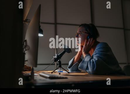 Una donna di mezza età in cuffie chiuse gli occhi e godeva di musica di qualità utilizzando un computer da tavolo. Studio di Home Sound moderna tecnologia di registrazione audio Foto Stock