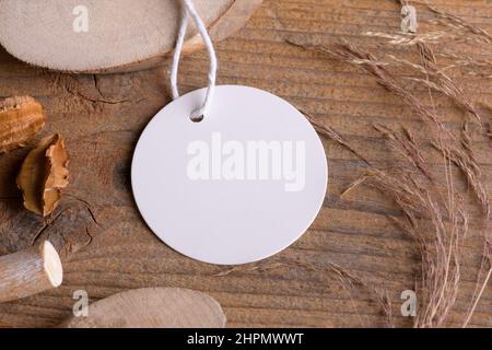 Tondino bianco mockup tag su un rustico sfondo di legno con filo di cotone e decorazione boho, elemento per imballaggio, primo piano. Etichetta prodotto bohémien moc Foto Stock