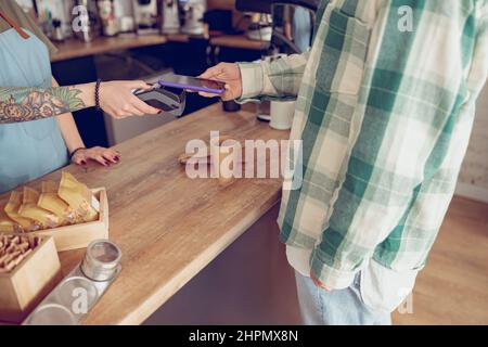 Cliente maschile che paga per il caffè con smartphone in caffetteria Foto Stock
