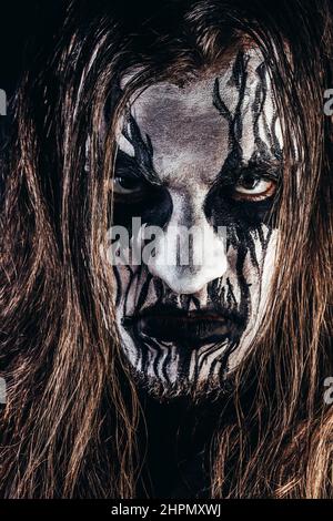 Foto ritratto di uomo in metallo nero con capelli lunghi e marrone e faccia dipinta su sfondo nero. Foto Stock
