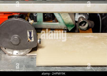 La lastra di gres porcellanato si trova di fronte ad una taglierina elettrica per piastrelle con disco da taglio diamantato e coperchio protettivo. Primo piano. Spazio di copia. Foto Stock