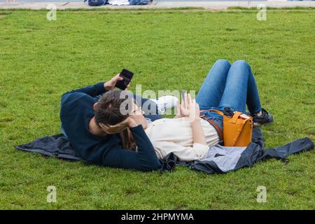 Inghilterra, Londra, Southwark, Potters Field Park, coppia che giace su Grass guardando gli smartphone Foto Stock