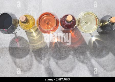 Vino rosso, bianco e rosato in bicchieri e bottiglie con ombre profonde su fondo di cemento e spazio per la copia. Concetto di vini. Foto Stock
