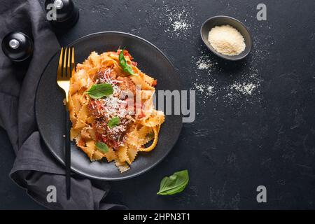 Tagliatelle con polpette di pomodoro, basilico e parmigiano su fondo di pietra nera o cemento. Piatti italiani e cucina tradizionale Foto Stock