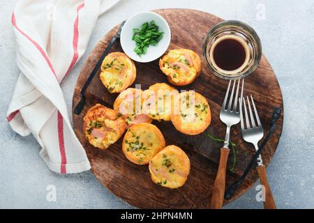 Deliziosi muffin alle uova con cipolle verdi, pancetta, formaggio e pomodori su tavola di legno su sfondo chiaro. Sana alta proteina e bassa colazione carb Foto Stock