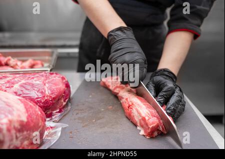 Primo piano di carne cruda e macellaio donna tagliando la carne con il coltello. Foto di alta qualità Foto Stock