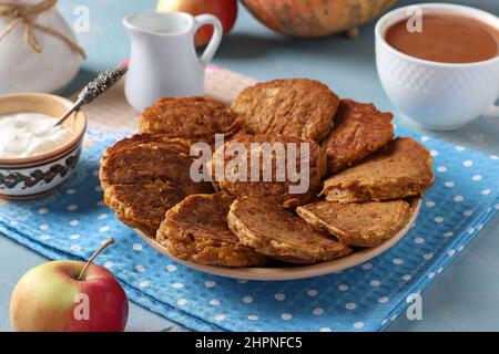 Frittelle di zucca e mele fatte in casa, servite a colazione con panna acida, nonché una tazza di caffè con latte su sfondo azzurro Foto Stock