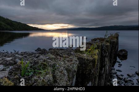 Guardando verso il basso Loch Rannoch sopra il molo sulla costa orientale, mentre il sole tramonta sulle montagne in lontananza, Rannoch, Scozia, Regno Unito. Foto Stock