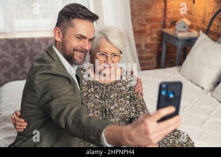 i parenti di mezza età portarono un figlio elegante con la madre anziana del pensionato che prendeva un selfie. Foto di alta qualità Foto Stock