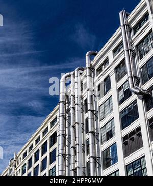 Vista ad angolo basso dell'esterno di un edificio industriale a più piani con un suggestivo cielo blu. Finestre e tubi di sfiato in argento. Foto Stock