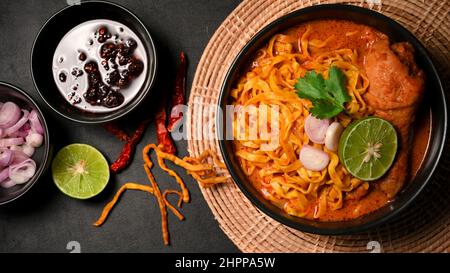 Colpo di testa, Khao Soi Kai servito con peperoncino in polvere fritto in olio, scalogni, lime e croccanti tagliatelle di uova fritte. Concetto di cucina Tailandese Settentrionale Foto Stock