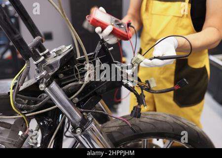 Il meccanico che utilizza un multimetro controlla il livello di tensione della batteria del motociclo nel garage del motociclo Foto Stock