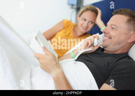 Una giovane coppia in camera d'albergo a letto chiama l'addetta al ricevimento al telefono Foto Stock