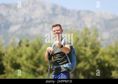 L'uomo con bastoni finlandesi per il nordic walking tiene i pollici in cima alla montagna Foto Stock