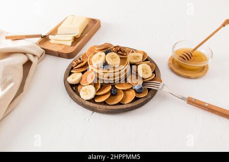 un piatto di legno rotondo con un sacco di pancake e una pila di pancake spessi: burro, miele, noci, frutta per migliorare il gusto Foto Stock