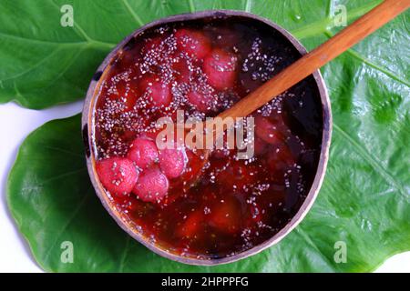 Vista dall'alto fragole rosse zuccherate in ciotola che fanno da conchiglie di cocco su foglia verde, frutta rossa fresca da Lat per giorno d'estate, cibo yummy Foto Stock