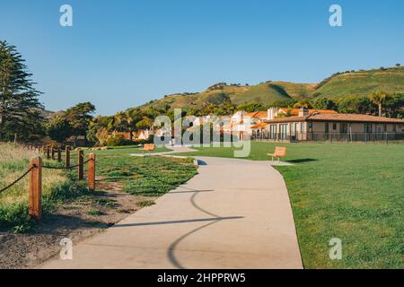 Lungo passerella lungo la riva, case con bel fronte paesaggistico il cortile e cielo blu chiaro sullo sfondo in una piccola città sulla spiaggia in California. Foto Stock
