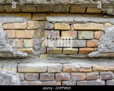 Mattoni in rilievo con intonaco sbriciolato. Frammento di un vecchio muro di mattoni. La texture del cotto di diversi colori. Primo piano. Messa a fuoco selettiva. Foto Stock