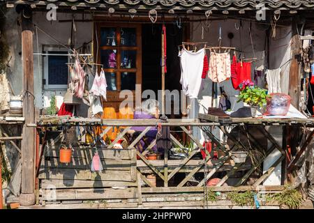 Donna seduta su un balcone stipato con vari oggetti, cercando di riscaldarsi nel sole d'inverno nel villaggio d'acqua di Wenzhou, Cina Foto Stock
