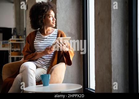 Pausa caffè con il tablet. Attraente donna d'affari nera che lavora su tablet digitale Foto Stock