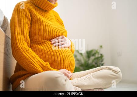 Una donna incinta carina si siede e tiene la mano sul ventre. Il concetto di una gravidanza felice in previsione di un bambino. 9 mesi di attesa per un bambino. Foto Stock