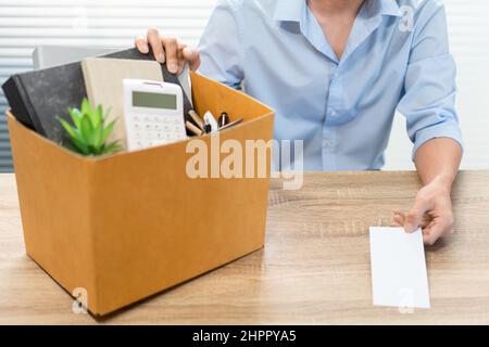 Concetto di dimissioni l'ufficiale maschile seduto, mettendo la sua scatola appartiene sulla scrivania e consegnando la lettera bianca a qualcuno. Foto Stock