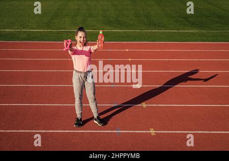 ragazza adolescente che tiene i barbells e la bottiglia d'acqua. allenatore di fitness si prepara per l'allenamento. riscaldamento sulla palestra dello stadio. potenza e forza. allenamento bambini a. Foto Stock