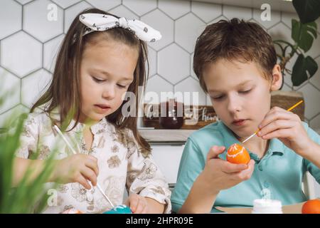 Ritratto di concentrato gioioso due bambini, ragazzo e ragazza, pennello pittura spazzola multicolore uova di galline pasquali su tavola di carta piatto. Rendendo bianco a Foto Stock