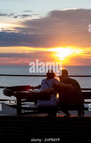 Coppia guardando il sole tramontare sul mare sulla costa orientale dell'Inghilterra a Hunstanton. Foto Stock