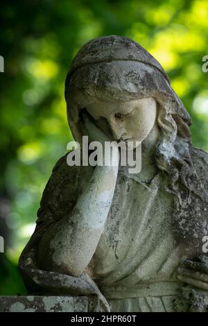 Un'antica statua in pietra di donna triste e disperata sulla tomba come simbolo della morte e della fine della vita umana. Foto Stock