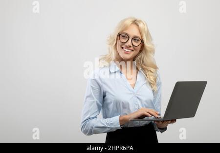 Felice giovane donna d'affari che usa il computer portatile contro lo sfondo grigio chiaro dello studio, guardando da parte lo spazio di copia Foto Stock