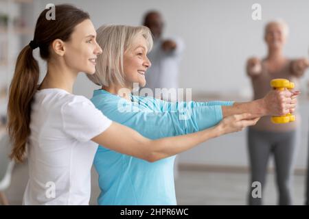 Vista laterale dell'allenatore di fitness che aiuta la donna anziana mentre si esercita Foto Stock