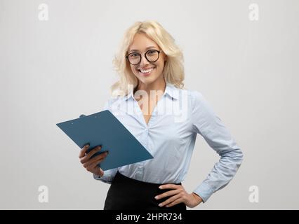 Ritratto di giovane donna d'affari di successo che posa con appunti in mano e sorridendo alla macchina fotografica Foto Stock