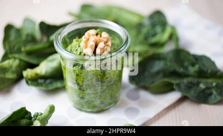 Pesto di noce verde in un vaso di vetro decorato con una noce e foglie sparse intorno Foto Stock