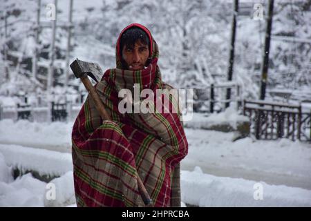 Kashmir, India , 23/02/2022, Srinagar, India. 23rd Feb 2022. Un lavoro cammina attraverso una strada coperta di neve durante la nevicata pesante in Srinagar.la maggior parte delle zone della valle del Kashmir il mercoledì ha ricevuto nevicata - la prima caduta pesante della stagione nelle pianure - interrompendo le operazioni di volo e di ferrovia e portando alla chiusura della strada nazionale vitale Srinagar-Jammu, i funzionari qui hanno detto. Credit: SOPA Images Limited/Alamy Live News Foto Stock