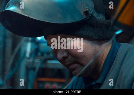 Ritratto di una saldatrice ad arco in argon con casco la testa sul posto di lavoro Foto Stock