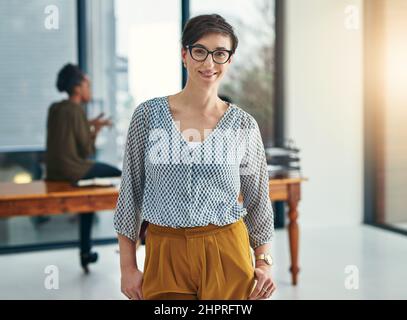 Una cosa di cui sono sicuri è il successo. Ritratto di un giovane creativo in piedi in un ufficio con i colleghi in background. Foto Stock