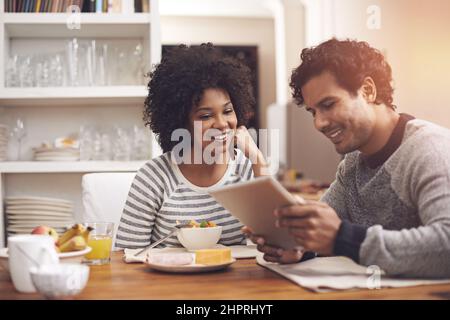 Iniziare la giornata insieme. Scatto di una coppia con un tablet digitale mentre si consuma la colazione a casa. Foto Stock