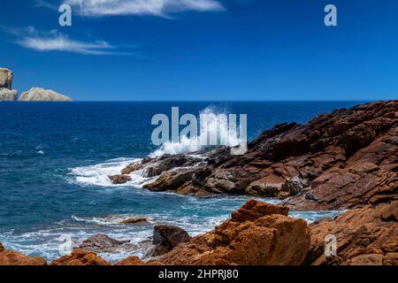 Un'onda colpisce le rocce e lo spruzzo vola nell'aria. Foto Stock