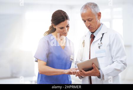 Confronto delle cartelle cliniche. Foto di due professionisti medici che guardano un tablet digitale. Foto Stock
